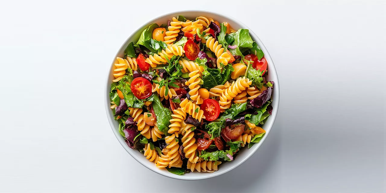 Aufsicht auf eine weiße Schale mit Nudelsalat, Tomaten und Blattsalat.