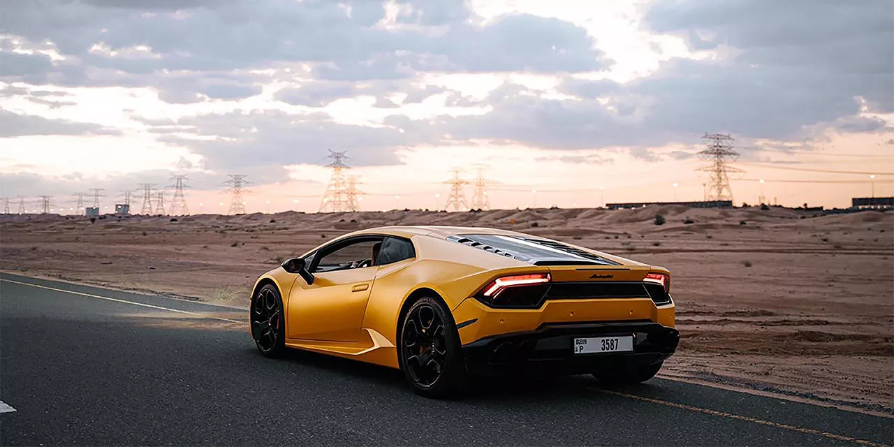 Ein gelber Lamborghini fährt auf einer Straße durch eine einsame, wüstenähnliche Landschaft.
